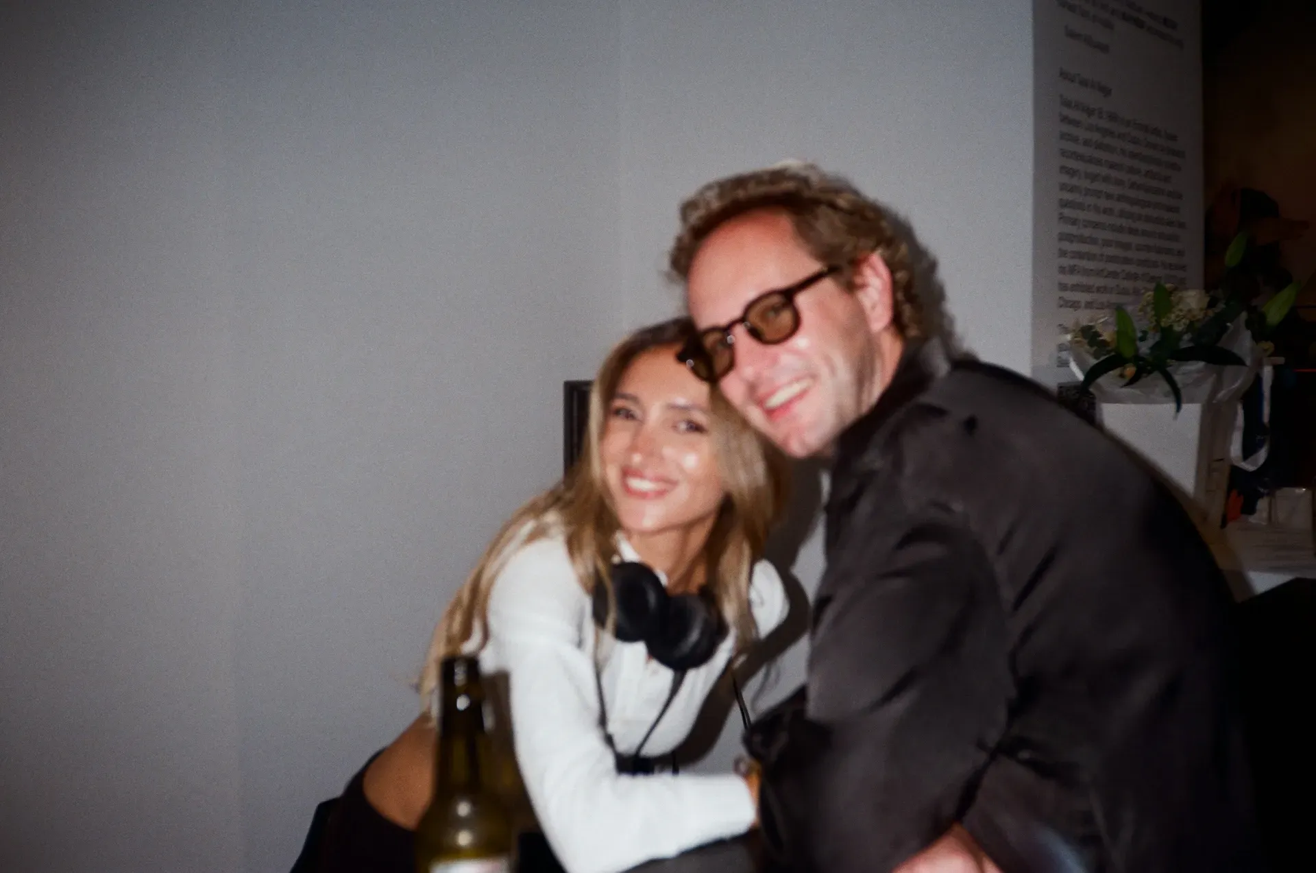 The DJ, headphones around her neck, sitting with a guest in glasses in front of the exhibition wall text