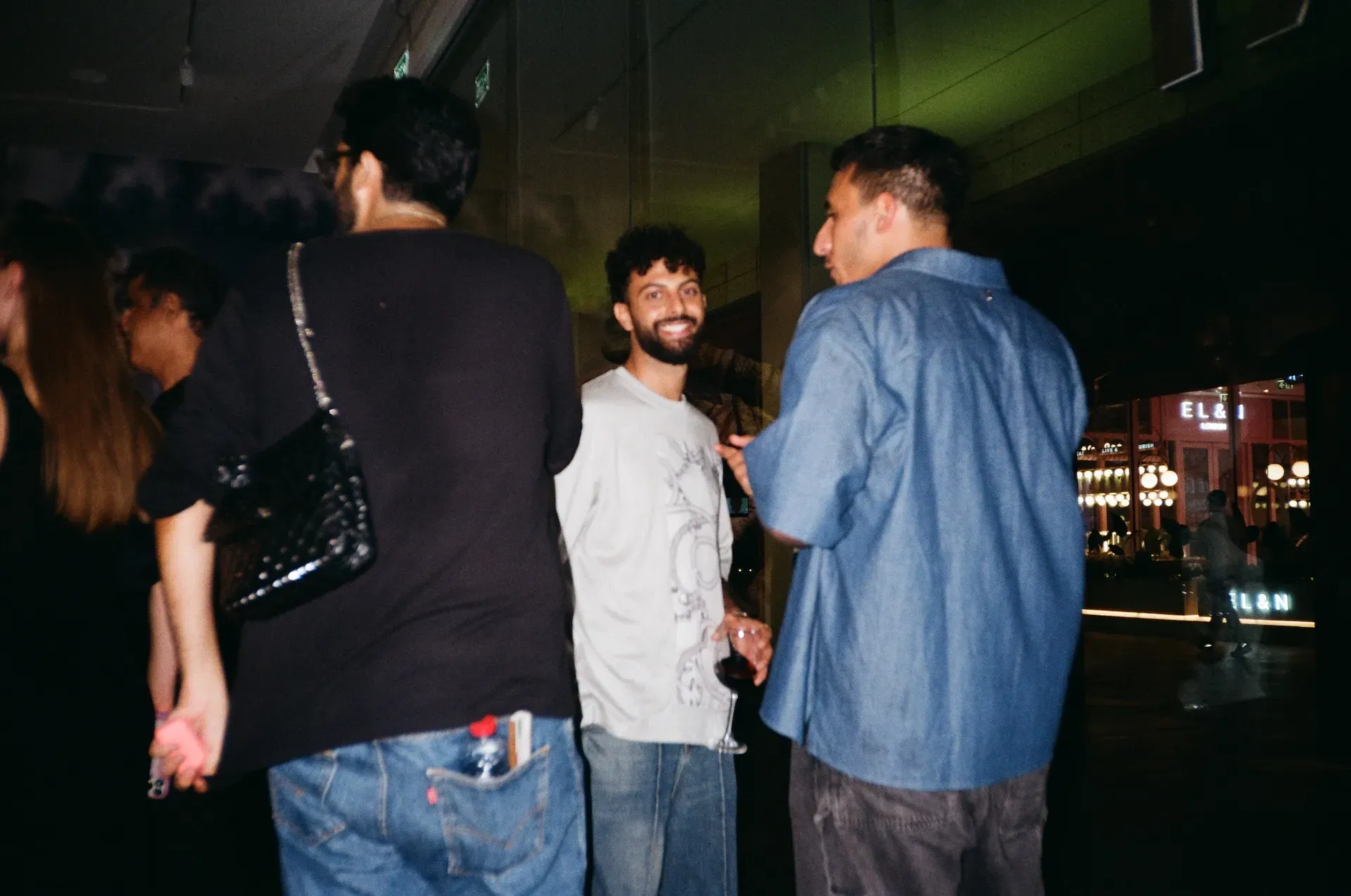 Three guests talking outside at night, with DIFC's lit storefronts in the background
