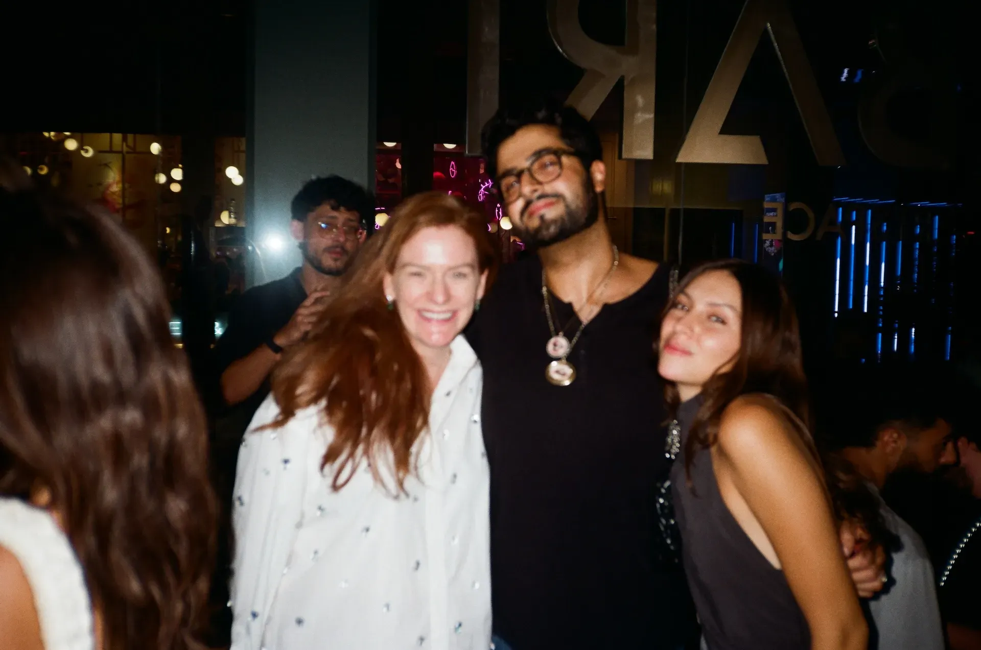 A group of four guests posing together outside at night near illuminated signage