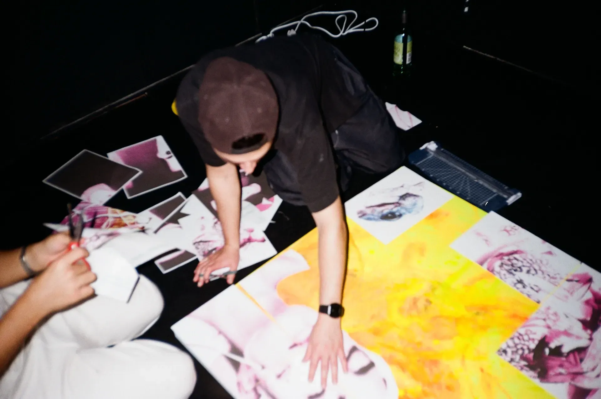 An artist arranging printed photographs and a yellow-painted canvas on a studio floor
